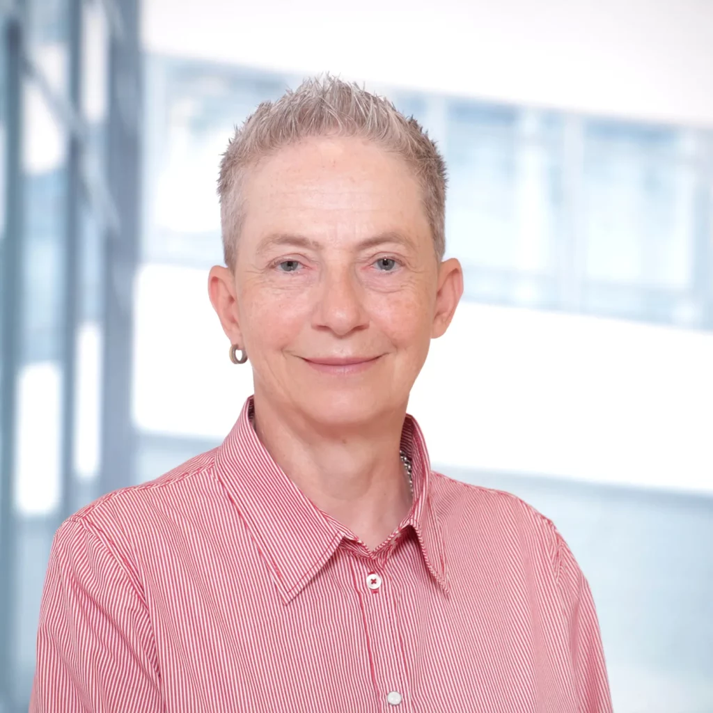 Portrait einer Person mit kurz geschnittenen Haaren in rot-weiß gestreiftem Hemd vor hellem Hintergrund.