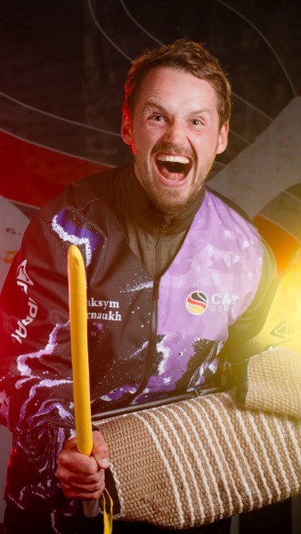 Maksym Karnaukh lacht ausgelassen in die Kamera und hält einen gelben Stock sowie den Gappay-Ärmelschutz; er trägt die schwarz-lila CACIT-Germany-Schutzdienstausrüstung vor dem CACIT-Germany-Backdrop.